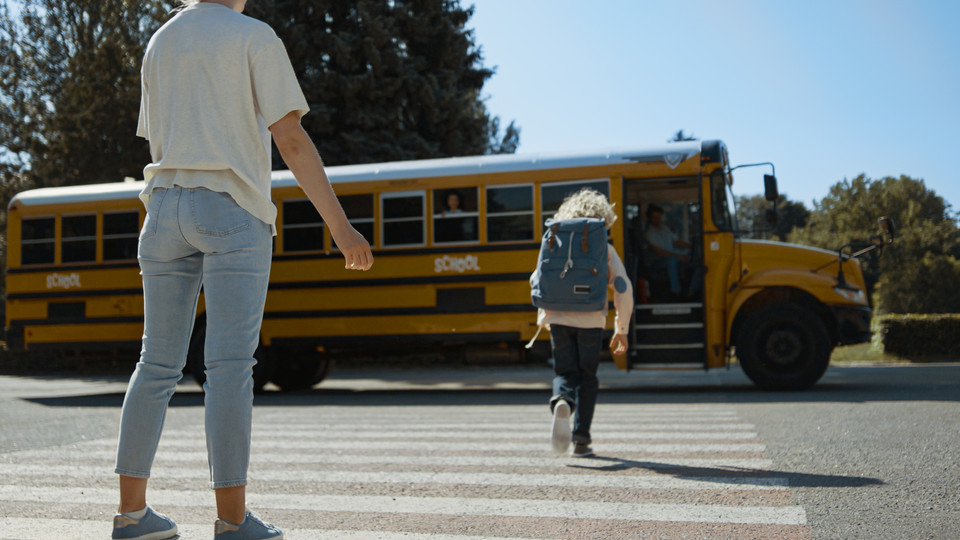 Parent watches child walk toward yellow school bus