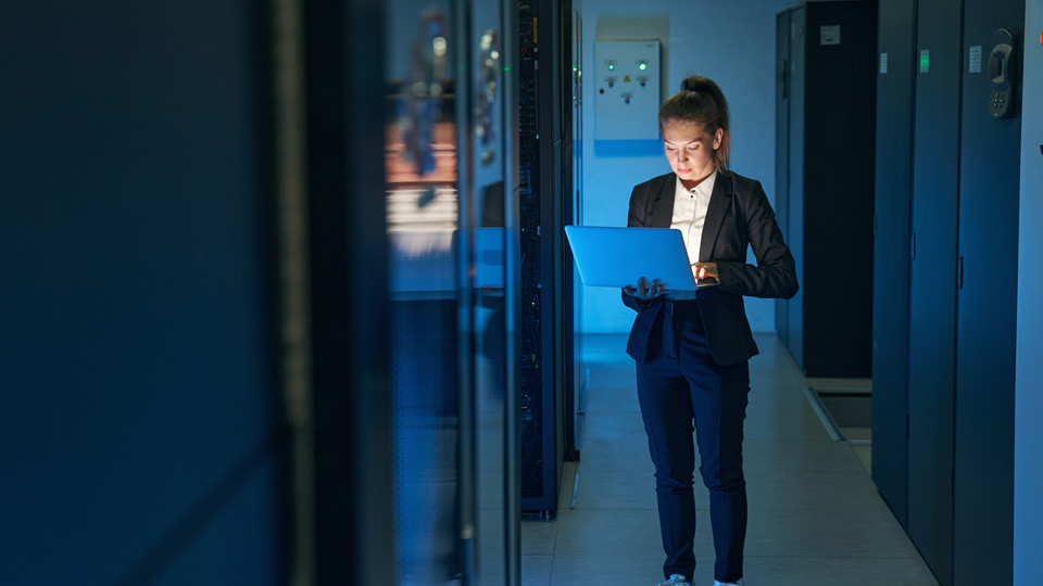 Woman looks at laptop in server room.