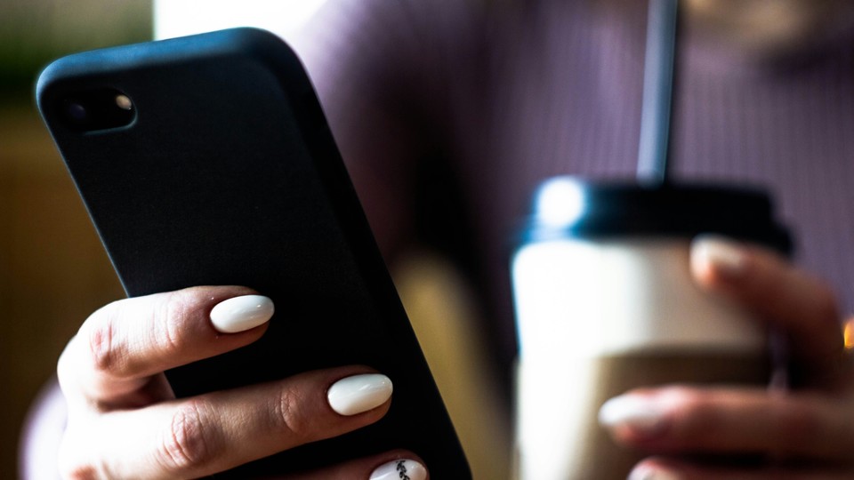 person looks at mobile phone and holds a coffee